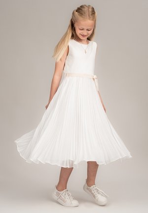 Weißes, plissiertes Kleid mit ärmellosem Design, einem beigen Taillenband und einem fließenden Rock. Kombiniert mit weißen Sneakers mit Spitzenakzenten.