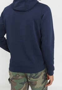 Marinblå hoodie med mjuk textur, justerbar huva och ribbad mudd, kombinerad med kamouflagemönstrade cargobyxor.