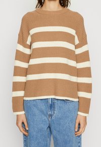 Mujer vistiendo un suéter de punto de rayas horizontales marrón y blanco combinado con unos jeans de tiro alto azul.