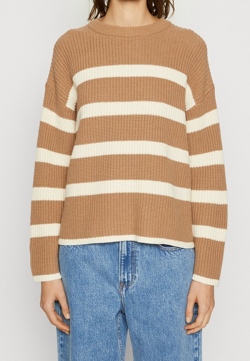 Mujer vistiendo un suéter de punto de rayas horizontales marrón y blanco combinado con unos jeans de tiro alto azul.