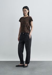 Brązowy t-shirt w panterkę z krótkim rękawem, zestawiony z czarnymi dżinsowymi joggerami z wysokim stanem, wyposażonymi w elastyczne ściągacze i standardowe kieszenie.