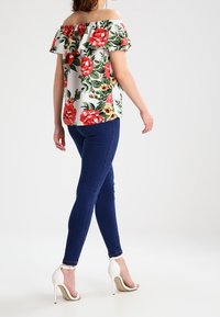 Kukkakuvioinen olkaimeton paita, jossa on punaisia ja vaaleanpunaisia kukkia valkoisella taustalla, yhdistettynä tummansinisiin kapeisiin farkkuihin ja valkoisiin korkokenkiin.