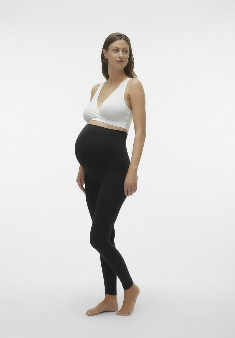 Graviditetsoutfit som innehåller en åtsittande svart leggins och en vit crossover-bralette. Slät tyg med en elastisk och bekväm passform.