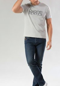 Camiseta gris de manga corta con texto negro y vaqueros de mezclilla azul. La camiseta tiene cuello redondo; los vaqueros presentan un corte recto clásico y detalle de botones.