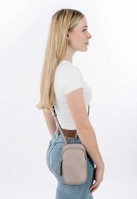 Grå läder crossbody-väska med en slät textur, smal rektangulär form och dragkedjestängning, bärs över en vit topp och blå jeans.