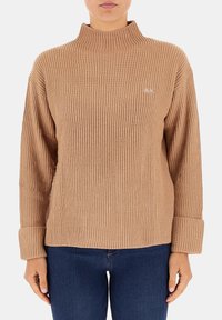 Maglione a collo alto ribbed marrone con maniche lunghe, polsini ripiegati e un piccolo dettaglio del logo sul petto. Texture morbida e vestibilità strutturata.