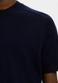 Chemise en maille bleu marine à manches courtes, dotée d'un col rond et d'une texture douce, avec des détails de couture subtils aux épaules.