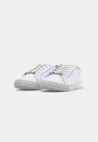 Sneaker bianche in tela con punta tonda, lacci piatti, suola in gomma testurizzata e marchio discreto sul lato. Finitura liscia e design minimalista.