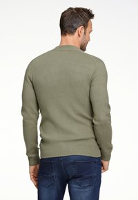 Maglione lavorato a maglia verde oliva con polsini e orlo a coste, visto da dietro. Design aderente abbinato a jeans blu scuri.