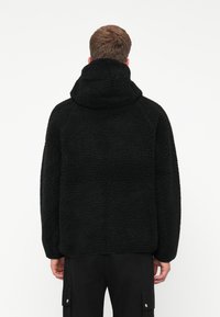 Moletom preto de fleece com superfície texturizada, capuz grande e corte descontraído. Apresenta mangas longas e barra arredondada.