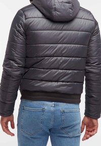 Puffjacka i matt svart, med horisontell sömnad, huva och ribbade muddar. Matchas med bleka blå denimjeans.