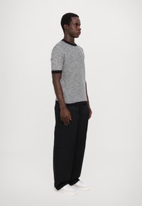 Korte mouwen grijs gebreid trui met marineblauwe afwerking, gecombineerd met brede zwarte broek en witte sneakers. Model staat tegen een effen witte achtergrond.
