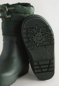 Bottes étanches vertes avec une semelle en caoutchouc texturée présentant un motif de goutte amusant. La tige est dotée d'un poignet froncé et d'un lacet ajustable.