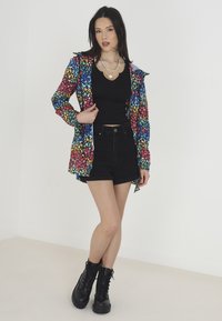 Chemise oversized colorée et à motifs avec une base noire, ornée d'un imprimé léopard vif. Assortie à un débardeur noir ajusté et à un short taille haute.