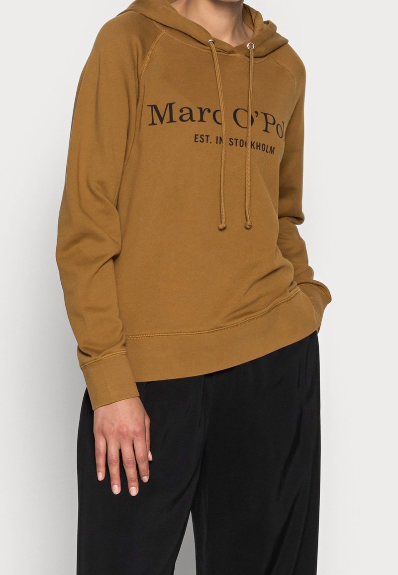 Sudadera con capucha marrón con texto de logo negro y detalles de cordón, con un corte relajado y puños acanalados. Textura de tela suave.