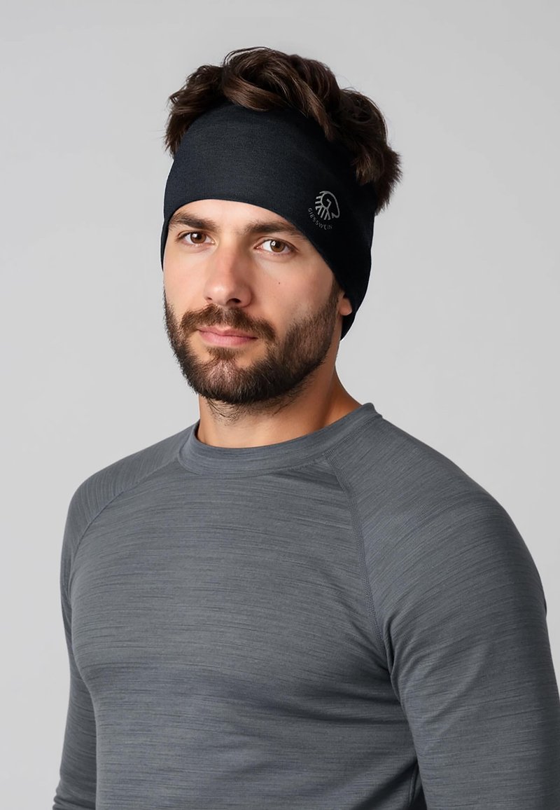 Bandeau noir avec des détails de couture et un logo sur le côté, porté par un homme en chemise grise à manches longues. Texture du tissu lisse.