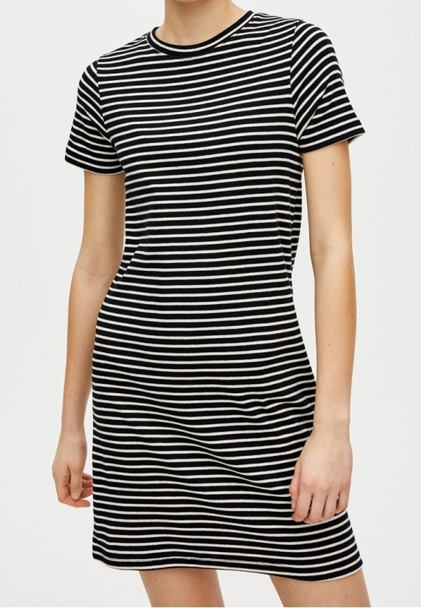 Femme portant une robe courte à manches courtes rayée horizontalement en noir et blanc, longueur genou, sur un fond uni.