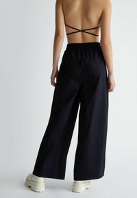 Navy spodnie o szerokich nogawkach z elastycznym pasem, wykonane z lekkiego materiału; cechują się płaskim przodem, bocznymi kieszeniami i luźnym krojem.
