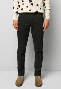 Schwarze Hosen aus einem Baumwoll-Mischgewebe, im Slim-Fit-Schnitt, mit zwei vorderen Taschen, getragen mit braunen Wildlederstiefeln.