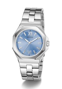 Srebrna metalna ura z osemkotno ohišje, modrim številčnico, rimskimi številkami in srebrnimi kazalci na povezani metalni zapestnici.