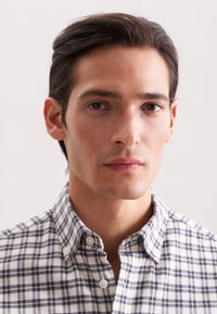 Camicia a maniche lunghe con una stampa a scacchi bianca e blu navy, dotata di colletto e tessuto dalla superficie liscia. Vestibilità ordinata attorno al collo.
