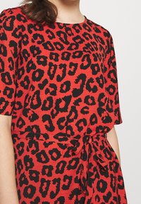 Robe rouge avec un imprimé léopard noir, dotée de manches courtes et d'un lien à la taille. Confectionnée en tissu texturé avec une coupe décontractée.