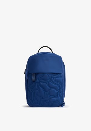 Zaino blu con motivo astratto trapuntato, maniglia superiore, tasca frontale con cerniera e cerniera del comparto principale su sfondo bianco semplice.