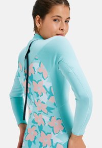 Light blue wetsuit with long sleeves, featuring a floral pattern in pink and teal on the lower back. Black zipper detail at the neck.