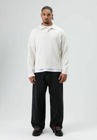 White knit pullover with a buttoned collar, paired with black wide-leg jeans. Black shoes with pink laces, smooth texture and relaxed fit.