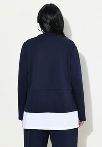 Top de manga larga azul marino con un ajuste relajado, que presenta un escote redondo y un detalle de dobladillo blanco en capas. Textura suave y diseño minimalista.
