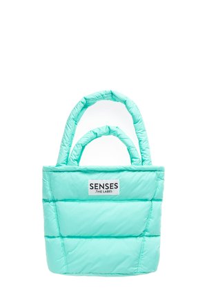 Hellblaue gesteppte Tragetasche mit zwei gepolsterten Griffen und einem weißen Etikett mit der Aufschrift "SENSES .THE LABEL" auf der Vorderseite.