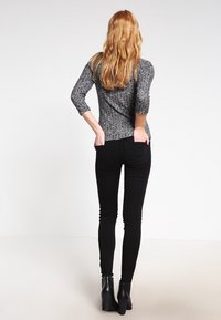 Czarne skinny jeans połączone z szarym, długim topem o fakturze, widok z tyłu. Charakteryzują się dopasowanym krojem i subtelnymi wzorami.