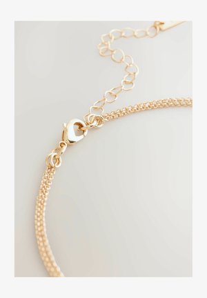 Kuldse tooniga käevõru, millel on peene ahel, väikesed ümmargused lingid ja vähkklambri sulgur. Sile tekstuur ja õrn sära.