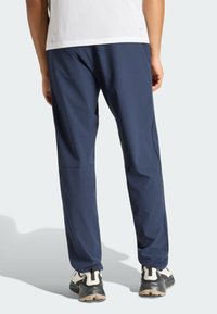 Marineblaue Sporthose aus leichtem Stoff, mit lockerem Schnitt, elastischem Bund und glatter Textur. Auffällige seitliche Taschen sind sichtbar.