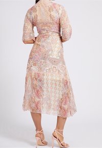 Maxi sukienka w pastelowych kolorach z wzorem w paisley i geometrycznym, wykonana z przezroczystego materiału, z półrękawami i zwiewnym krojem. Różowe sandały na obcasie z paskami.