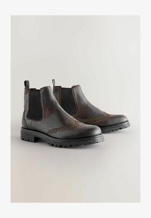 Braune Chelsea-Boots aus Leder mit seitlichen Mesh-Einsätzen, Broguemuster und strukturierten schwarzen Gummisohlen. Mit Schlaufe an der Ferse für einfaches Anziehen.