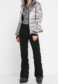 Silvrig pufferjacka, dragkedja, hög krage, svarta accenter, ihopparad med svarta byxor, isolerande material, stilren design, lättviktig.