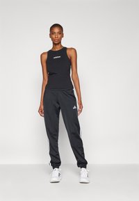 Top preto de alças com o logótipo da Adidas, combinado com calças de desporto pretas com riscas brancas nas laterais. Ambos os itens t�êm um design justo.