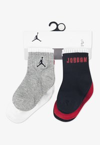 Dve pari gležnarskih nogavic: ene sive barve z belim robom in črnim logotipom; druge črne z rdečim napisom "JORDAN" in belim robom. Mehak tekstilni material.