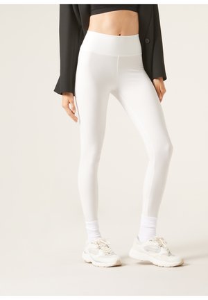 Hvide leggings med høj talje og en glat, strækbar tekstur, parret med hvide sneakers og en sort blazer.