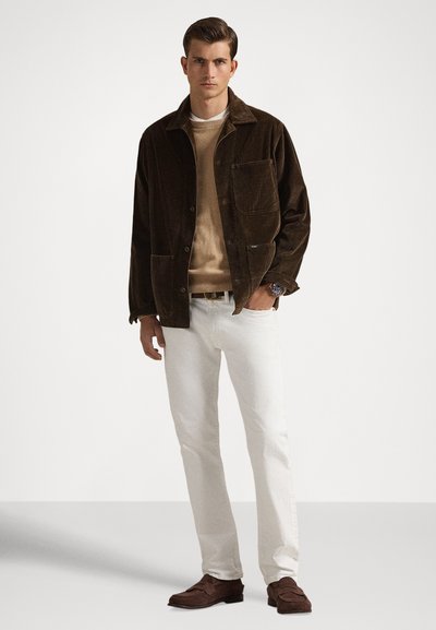 Καφέ ζακέτα από κορδόνι πάνω από μπεζ πλεκτό πουλόβερ, συνδυασμένη με λευκό παντελόνι και σκούρα καφέ παπούτσια. Διαθέτει τσέπη στο στήθος και κουμπιά.