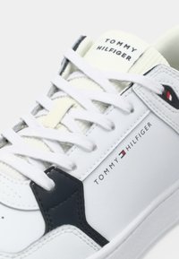 Bijela Tommy Hilfiger tenisica s bijelim vezicama, crnim i mornarsko plavim detaljima te logotipom branda na strani i jeziku.