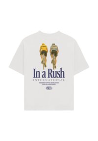 Deux cyclistes nommés Reimann et Krause roulant côte à côte, portant un t-shirt blanc avec les textes "In a Rush International" et "Modern Yuppies Worldwide Berlin Avantgarde".