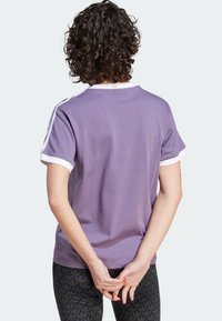 Lila kortärmad t-shirt med vit krage och ärmaccent, med en mjuk textur och avslappnad passform. Synlig ryggdesign och sömnad.