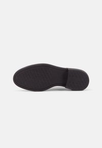 Semelle de chaussure en caoutchouc noir avec un motif texturé en zigzag, bout arrondi et bord lisse. Pas de branding visible ni de caractéristiques supplémentaires.