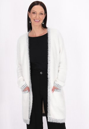 Strickjacke in Weiß mit schwarzem Streifenrand, offenen Front, langen Ärmeln und zwei Vorderaschen. Weiche, flauschige Textur.