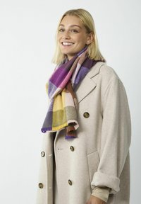 Multicolore sjaal met ruitpatroon in tinten paars, roze, geel en groen. Gemaakt van zachte stof met franjes. Een gelaagd uiterlijk over een beige jas.