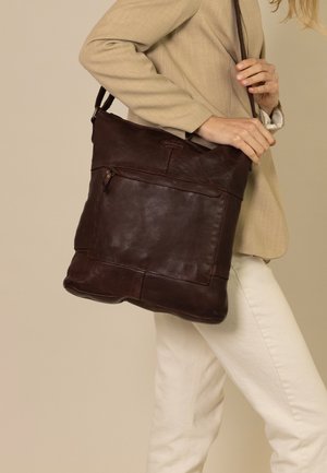 Braune Leder-Shopper-Tasche mit glatter Textur, einem Schulterriemen, Reißverschluss oben und einer vorderen Reißverschlusstasche. Quadratische Form mit genähten Akzenten.