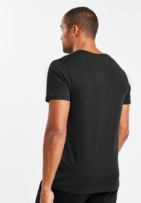 Tricou negru cu mânecă scurtă și gât rotund clasic. Fabricat dintr-un material moale, are o textură netedă și un design cu tiv plat.