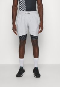 Pantalones cortos deportivos color gris claro con cintura ajustable, que presentan pantalones de compresión a rayas negras debajo y zapatillas de deporte negras.